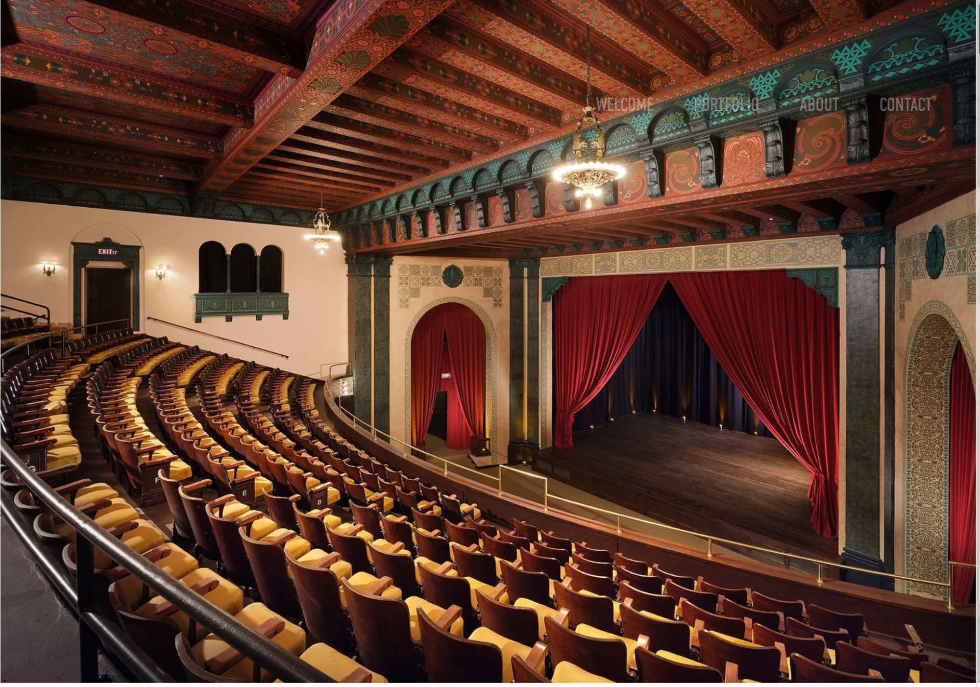 The image shows a vintage theater with ornate decorations, red curtains, rows of seats, and a wooden ceiling, creating a classic ambiance.