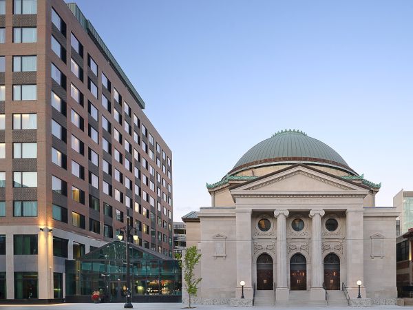 A historic domed building stands next to a modern multi-story structure under a clear sky.