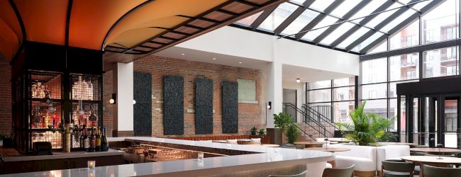 A modern bar with a sleek design, featuring a long counter, chairs, large windows, and an inviting atmosphere.