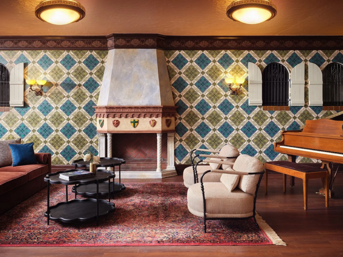 The image shows a stylish living room with patterned wallpaper, a fireplace, sofa, armchairs, stack tables, a piano, and a decorative rug.