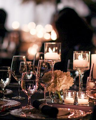 The image shows a dimly lit elegant dining setup with candles, wine glasses, and floral arrangements, creating an intimate atmosphere.